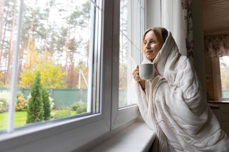 A women bundled in a blanket drinking from a coffee mug