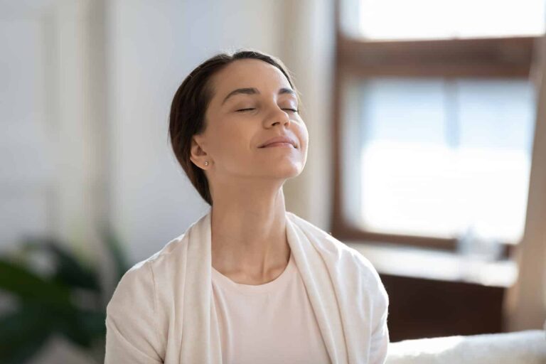 A content women sitting on sofa with closed eyes brathing air