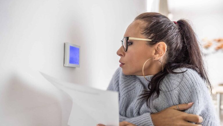 A cold woman looking at her home thermostat
