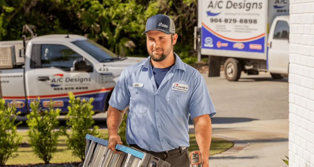 An A/C Designs HVAC technician approaching a house carrying a ladder.