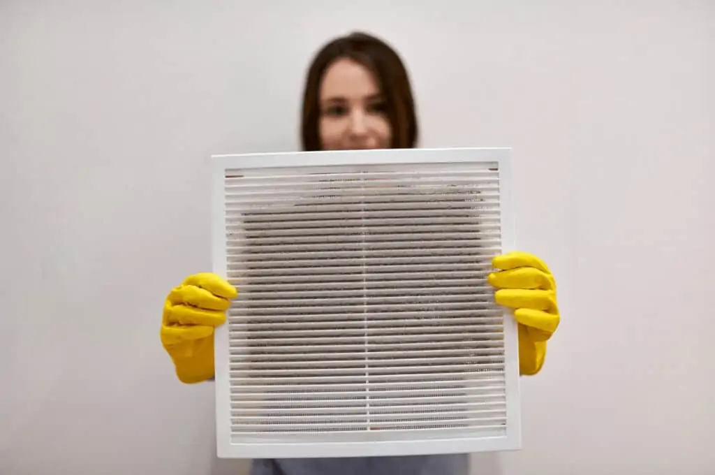 A woman holds a dirty air filter with gloves on