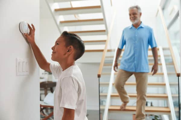 A young boy changes the home's thermostat and his father walks down the stairs