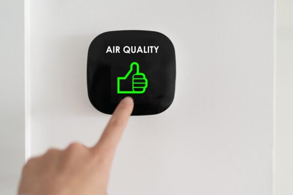 A person points their finger to a device on their wall that shows a green thumbs up and text reading "Air Quality"