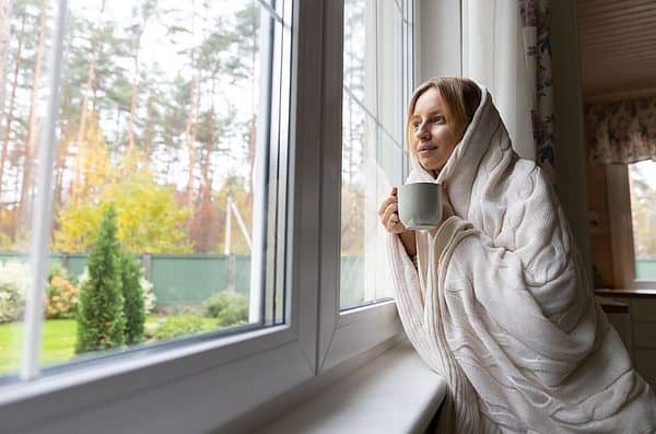 A woman bundled in a blanket drinking from a coffee mug