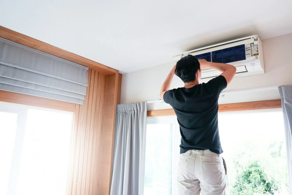 A man adjusts his air conditioning system on his wall