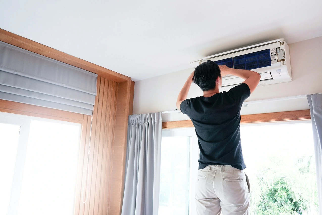 A man adjusts his air conditioner system on his wall