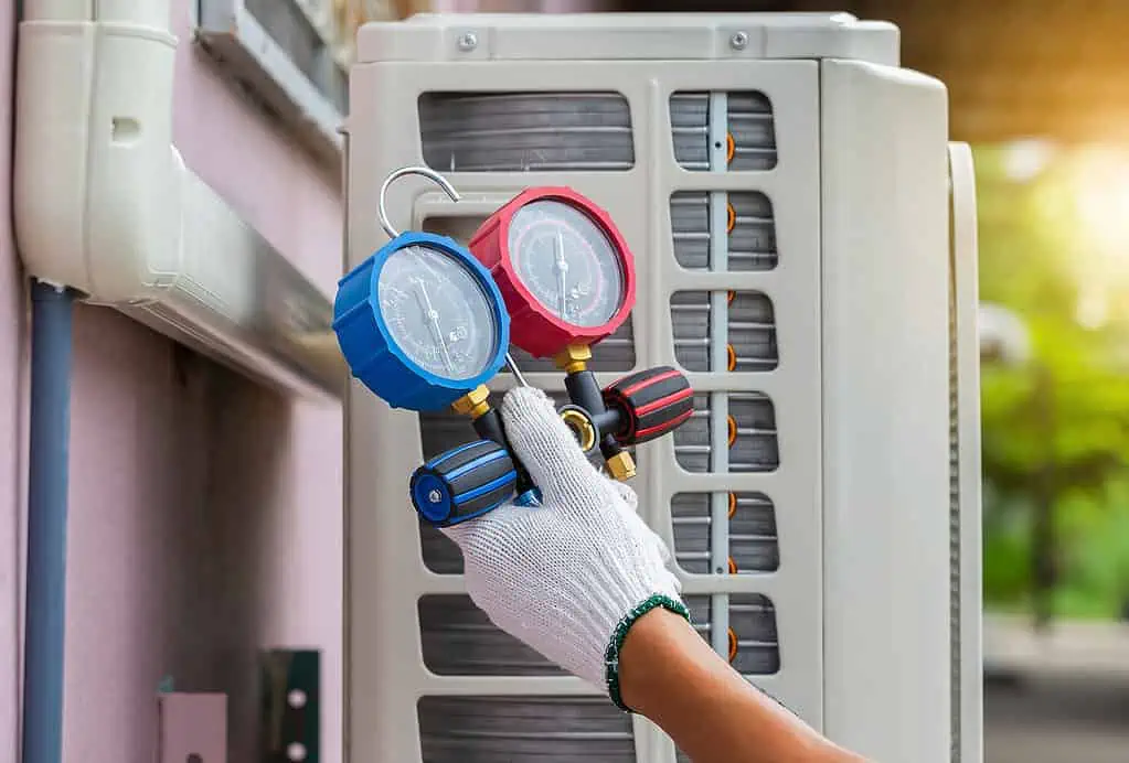 A technician holds a meter device next to an outdoor HVAC unit