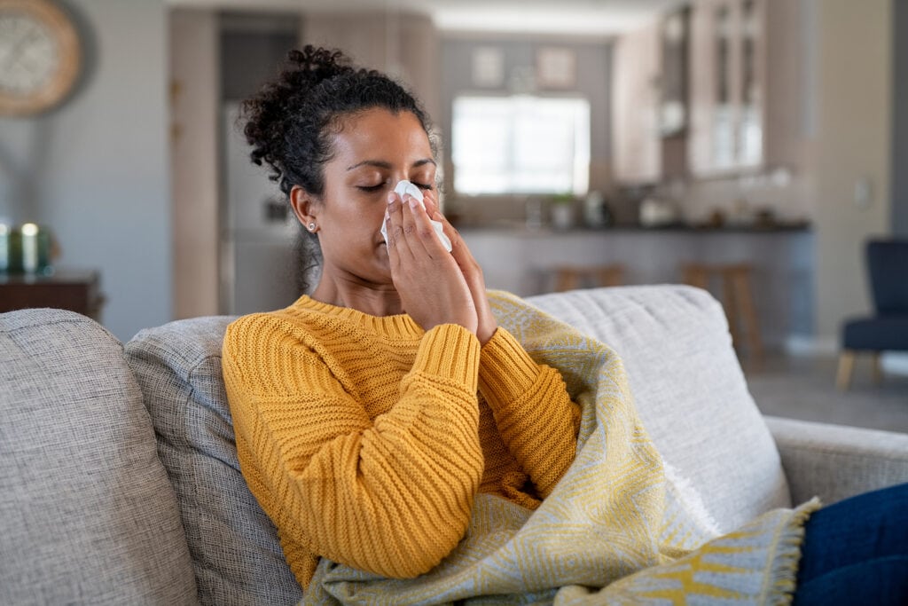 sick young woman sitting in home with hvac system blowing nose